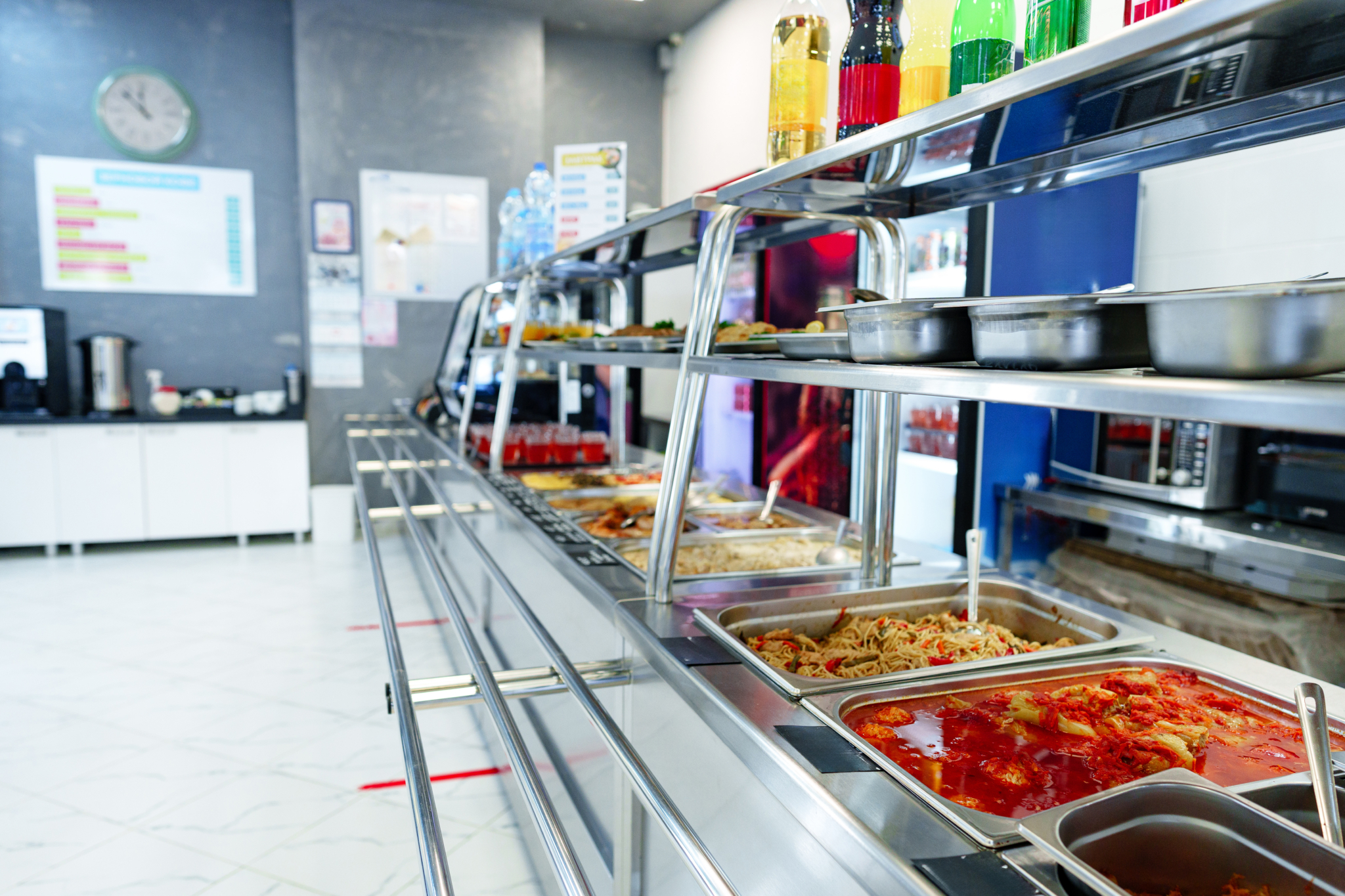 Photo of a cafeteria serving line filled with trays of hot food that are neatly arranged under the protective glass shield.